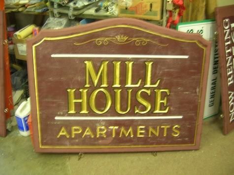 Sign for Mill House Apartments, brown and gold, with ornate detailing.