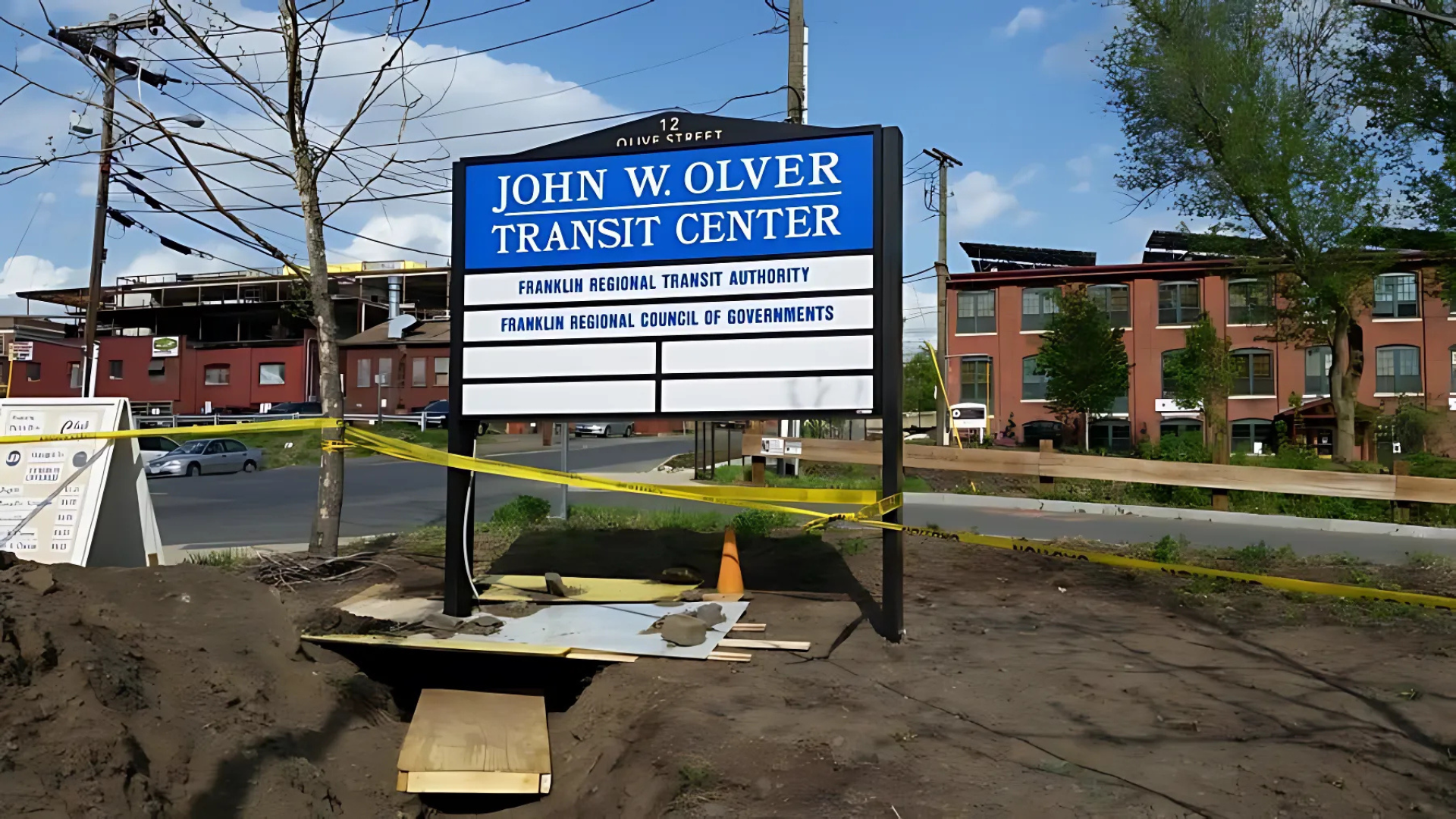 Sign for John W. Olver Transit Center in front of building and a partially dug-out ground with caution tape.