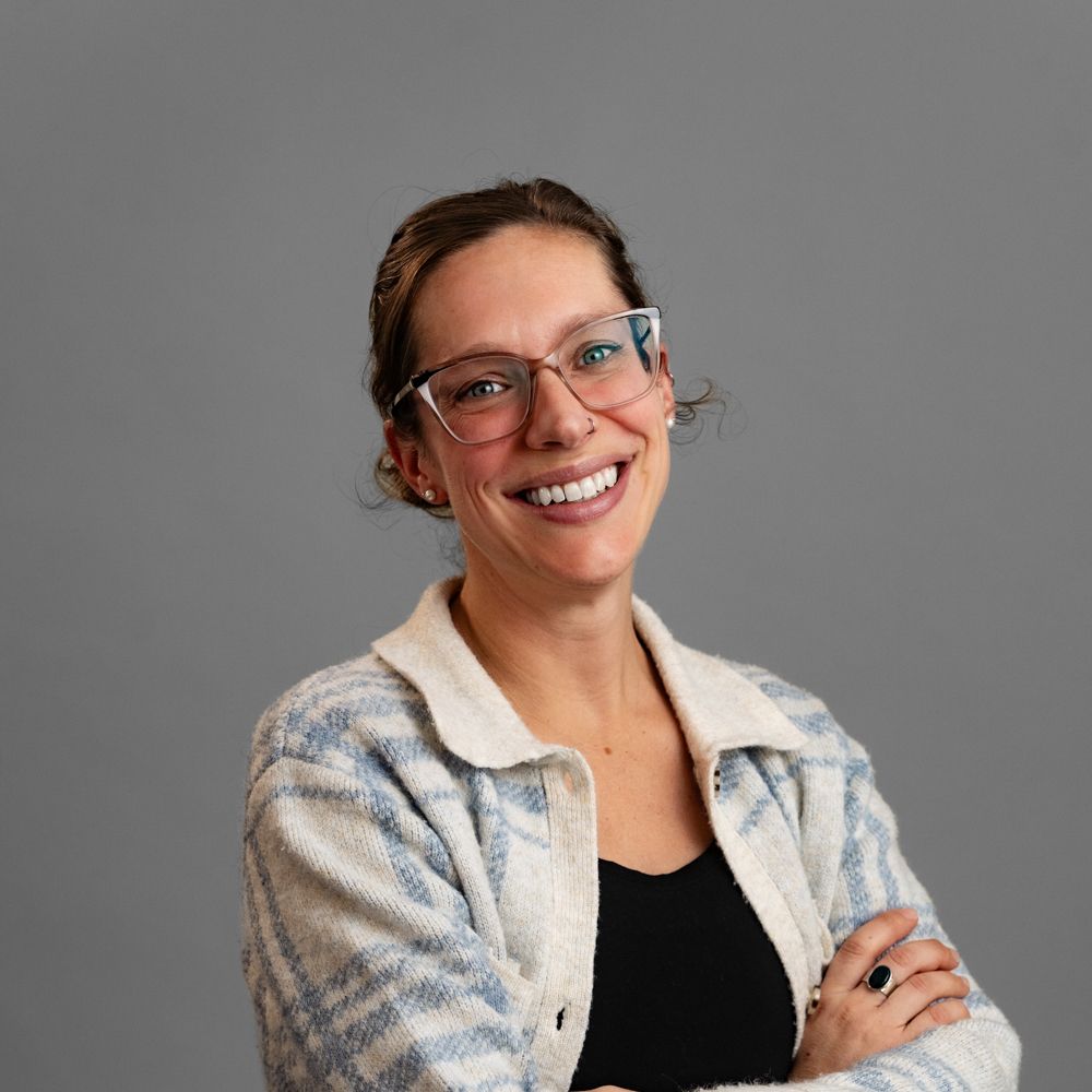 A woman wearing glasses and a plaid vest is smiling for the camera.
