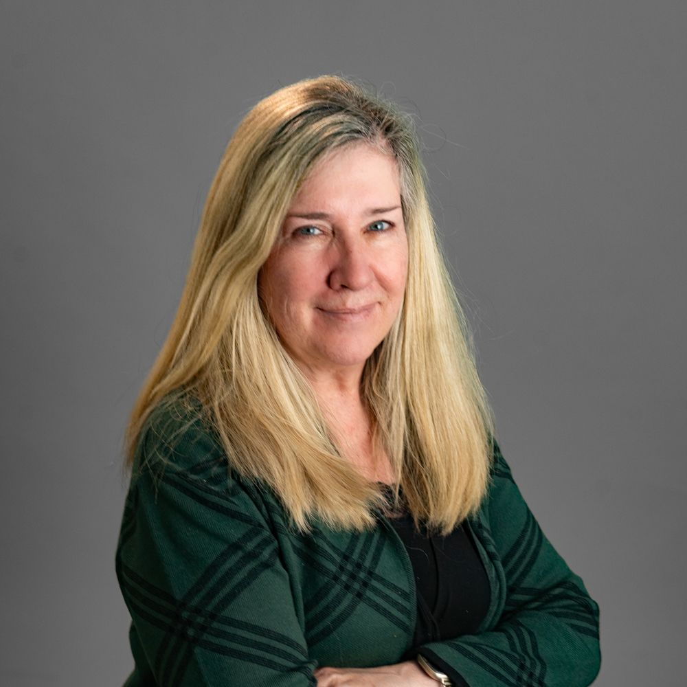 A woman with long blonde hair is wearing a blue cardigan and a black shirt.