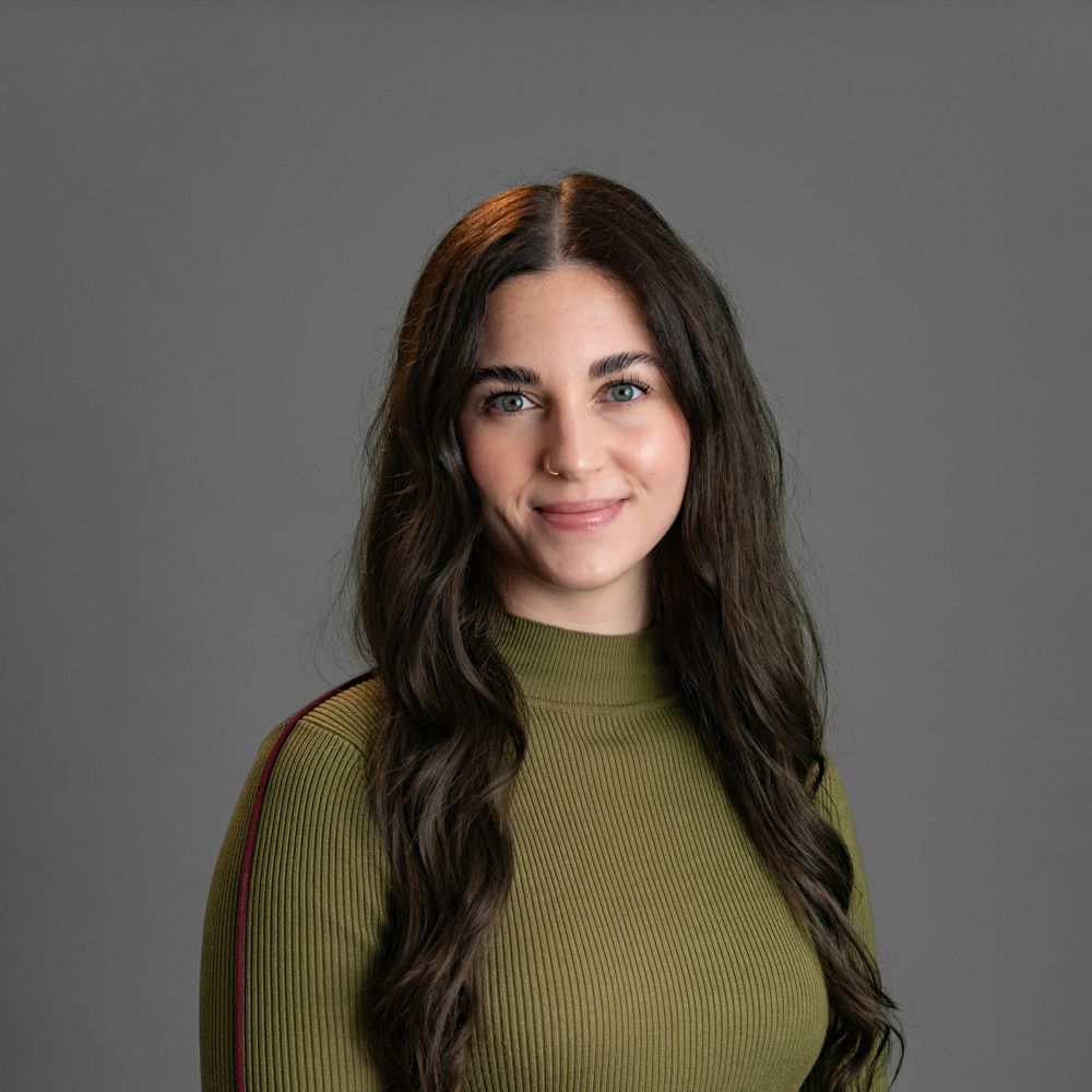 A woman wearing glasses and a grey sweater is smiling.