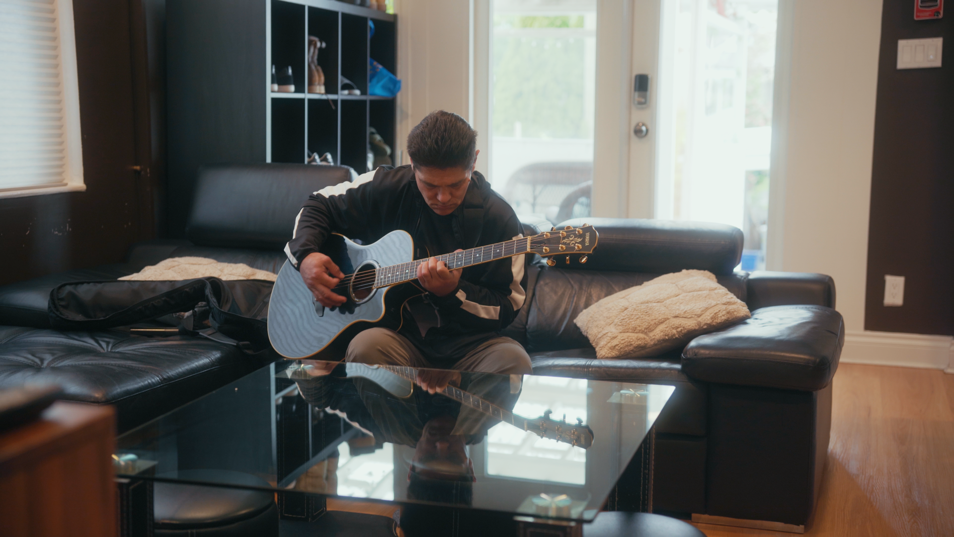 A man is sitting on a couch playing a guitar in a living room.