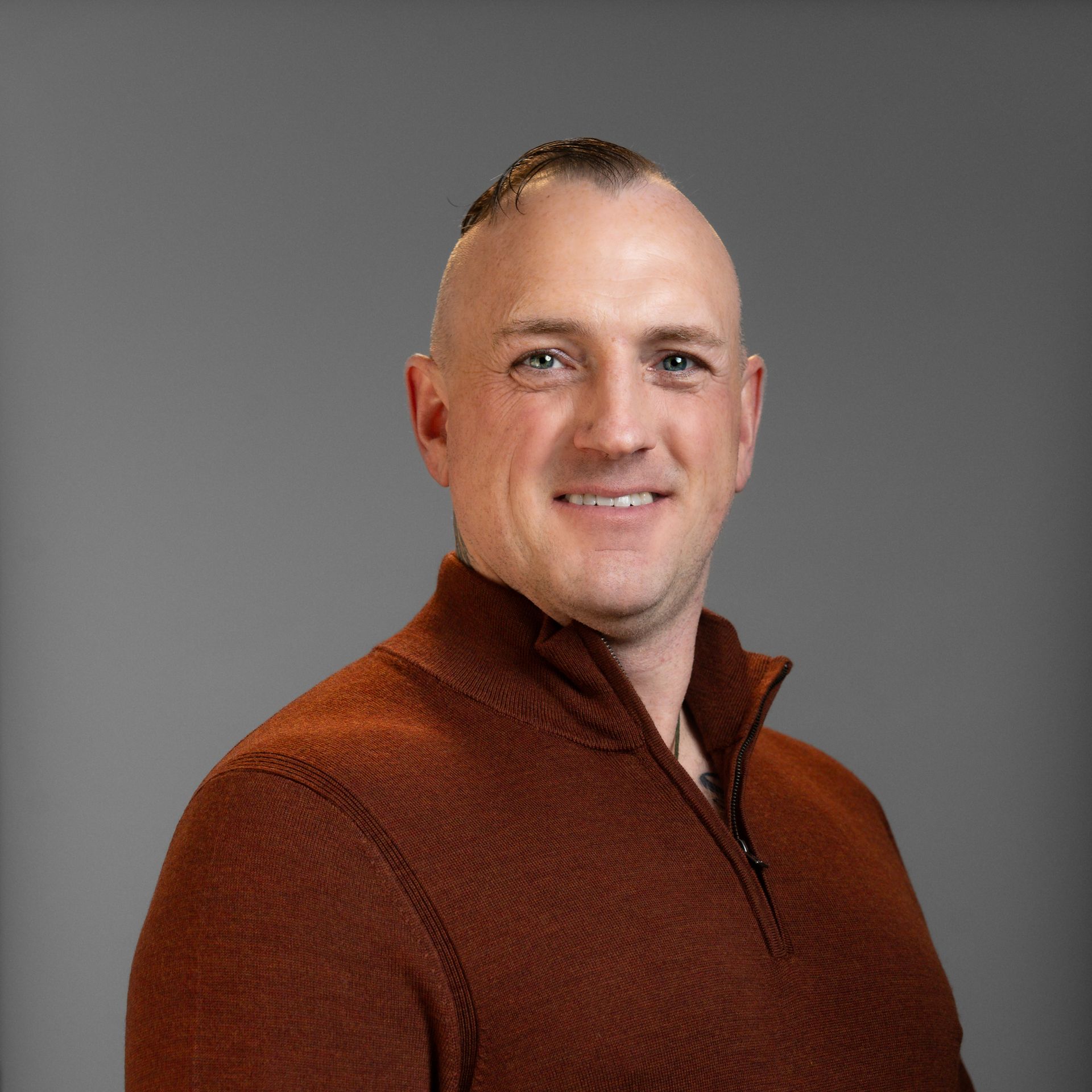 A man in a brown sweater is smiling for the camera.