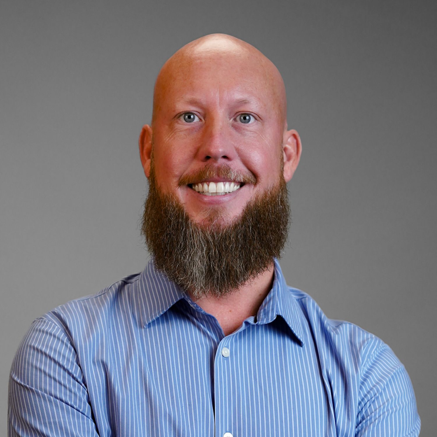 A bald man with a beard is wearing a blue striped shirt and smiling.