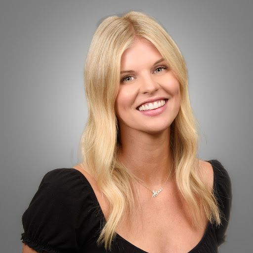 A woman with long blonde hair is wearing a black shirt and smiling.