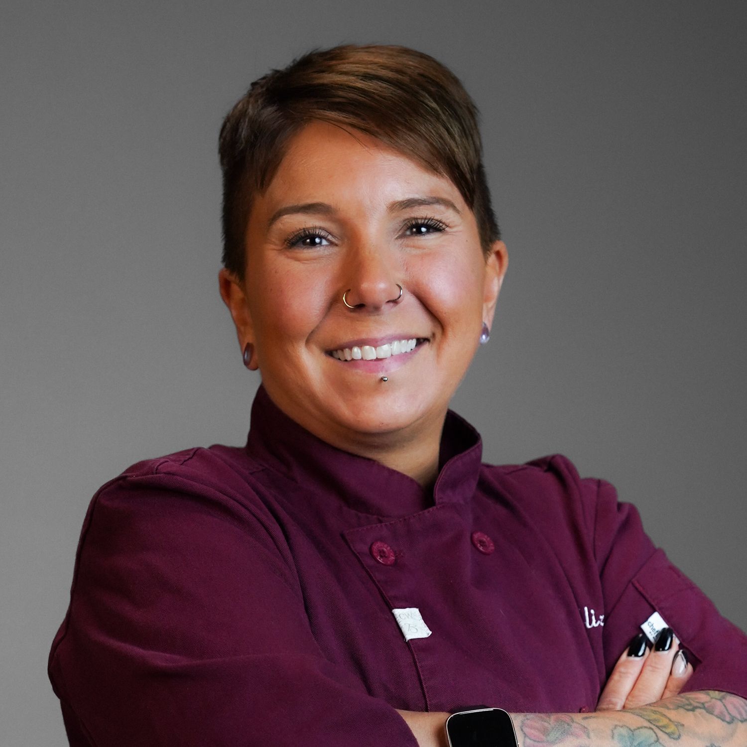 A woman in a chef 's uniform is smiling with her arms crossed