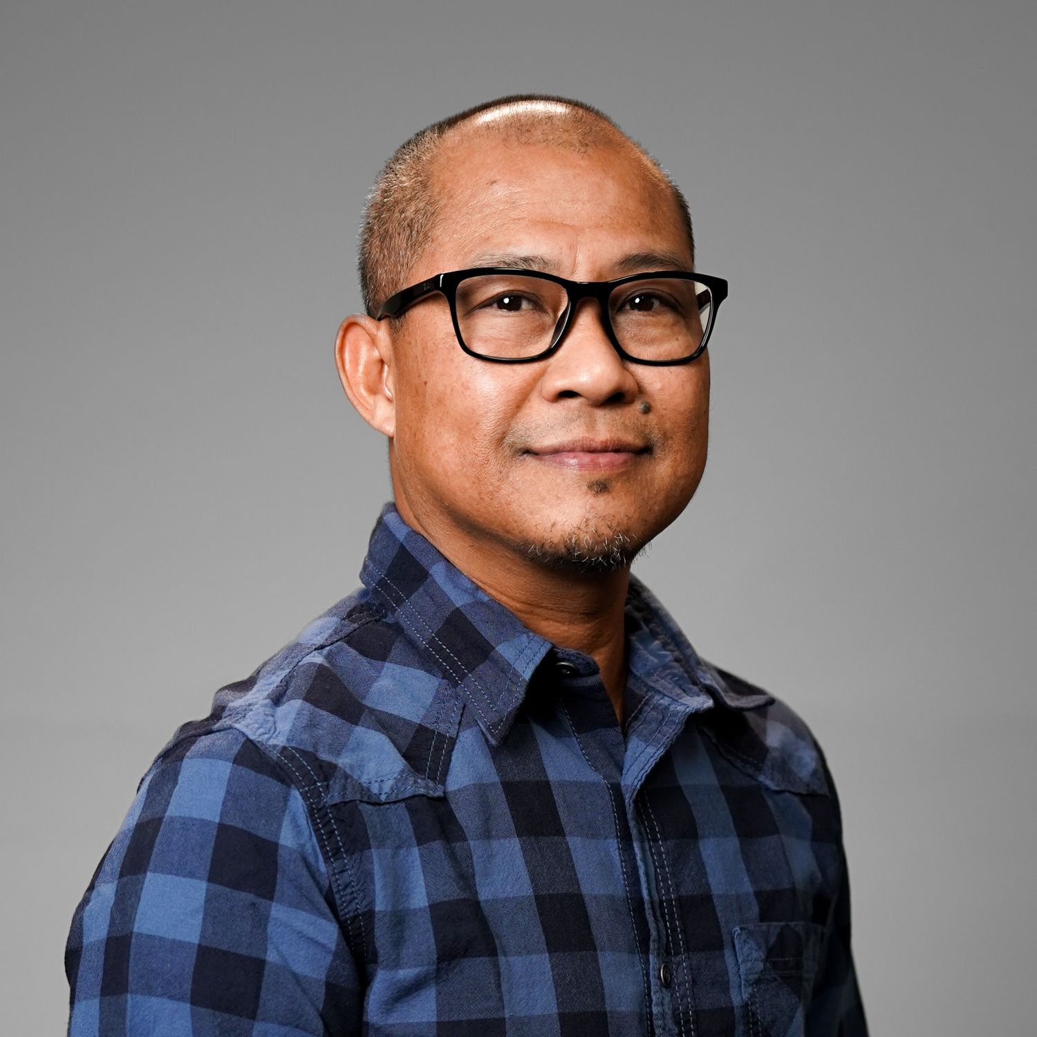 A man wearing glasses and a blue plaid shirt is smiling for the camera.