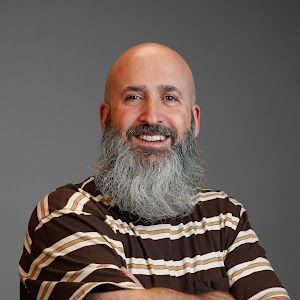 A bald man with a beard is wearing a striped shirt and smiling.