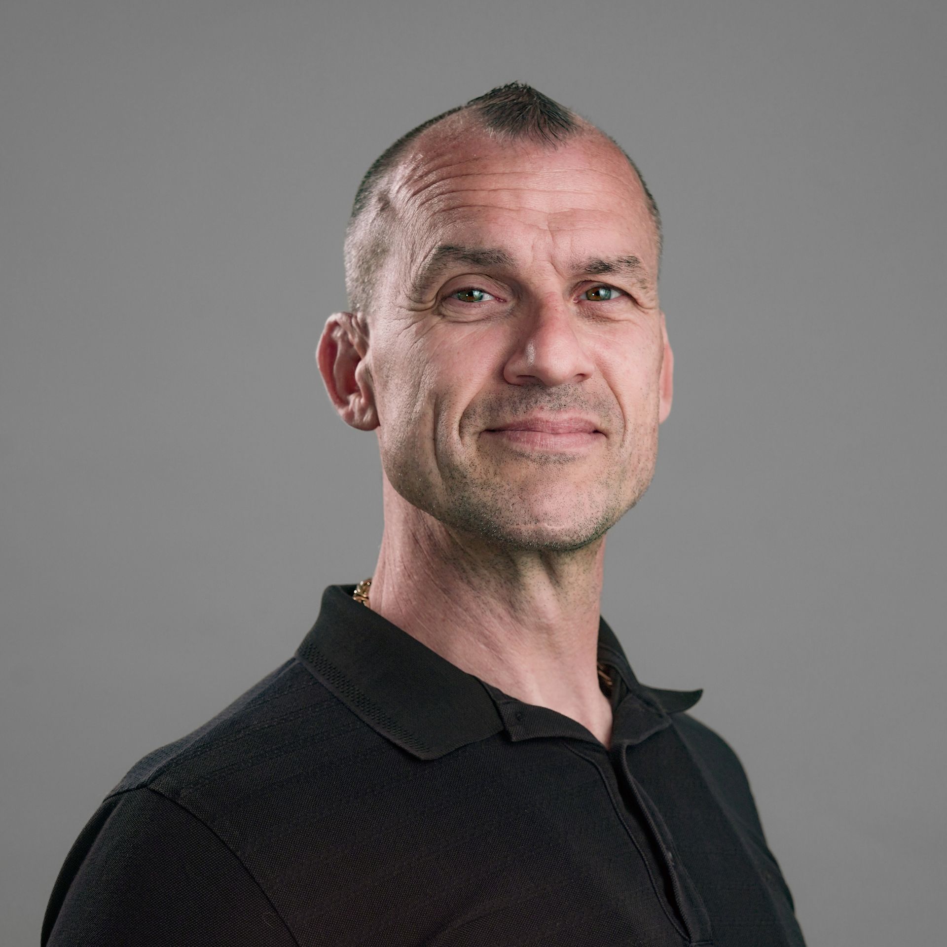 A man in a black shirt is standing in front of a white wall.