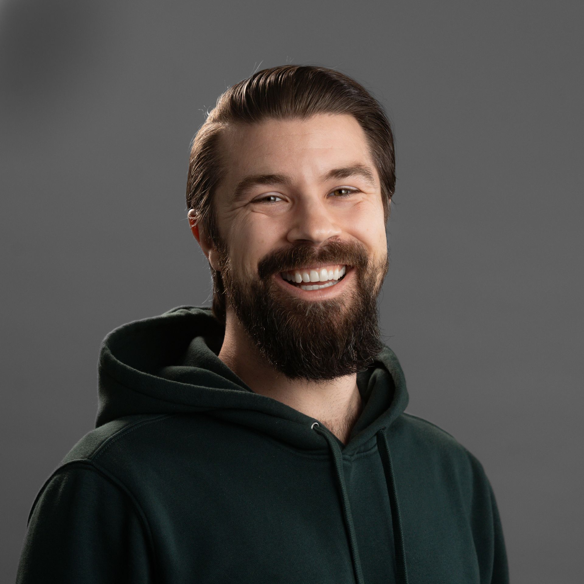 A man with a beard is wearing a green hoodie and smiling.