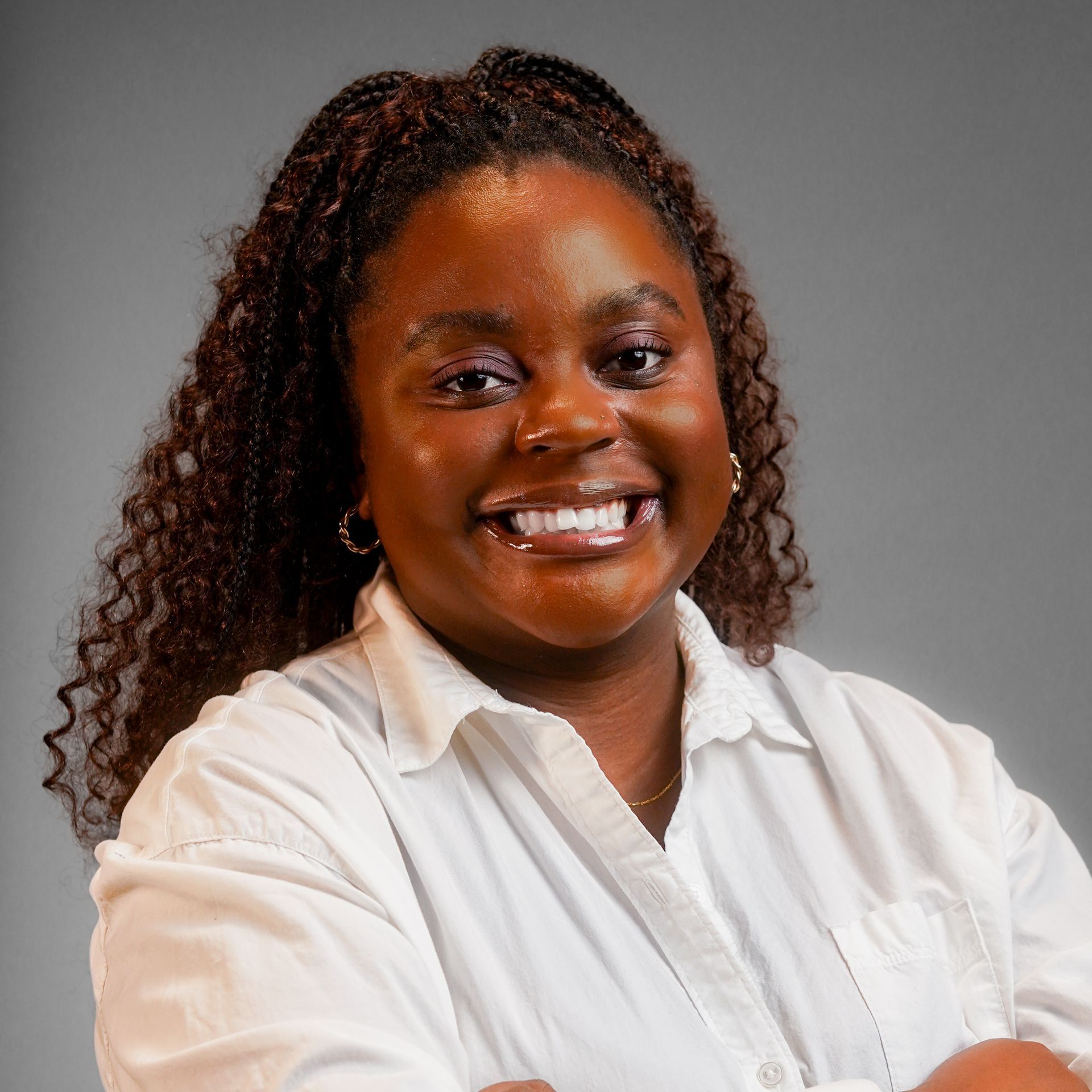 A woman with curly hair is wearing a white shirt and smiling.