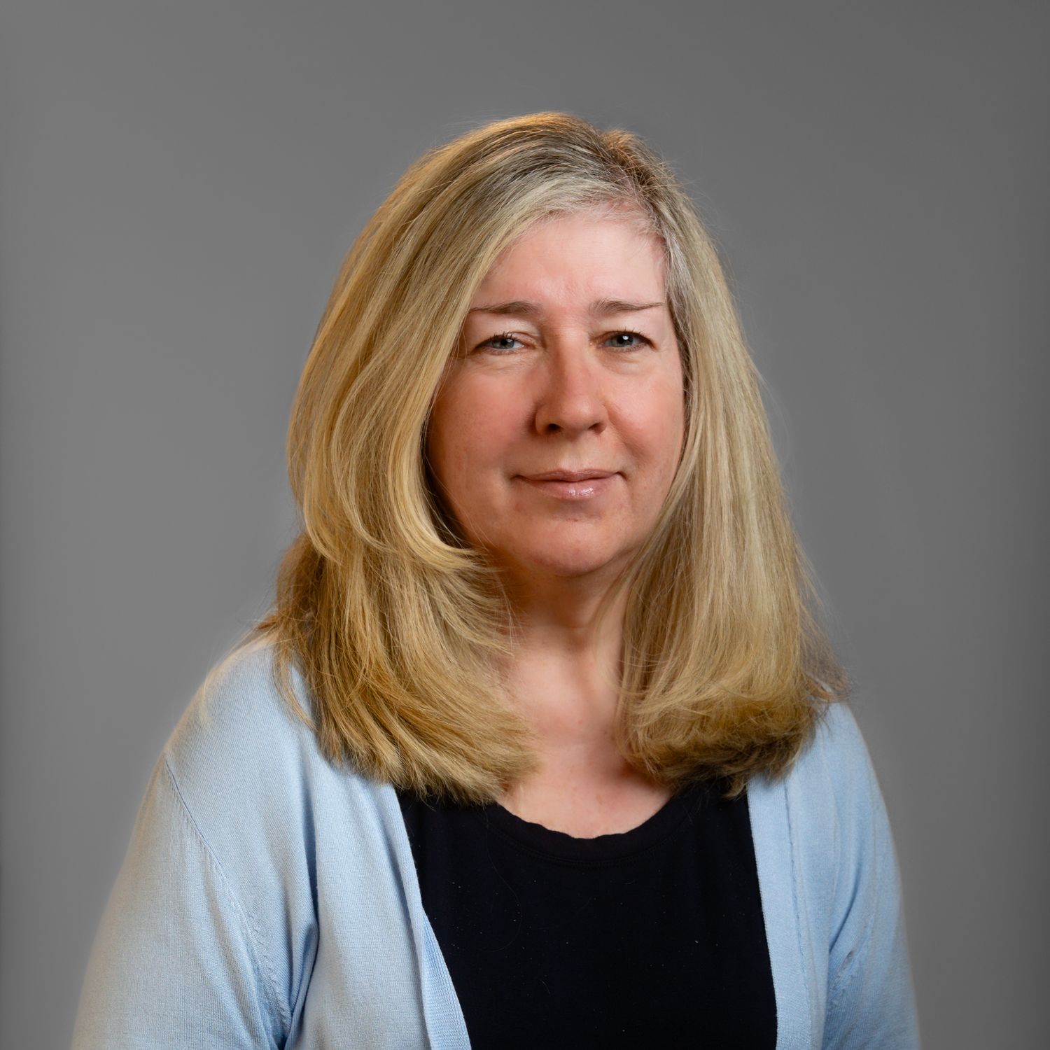 A woman with long blonde hair is wearing a blue cardigan and a black shirt.
