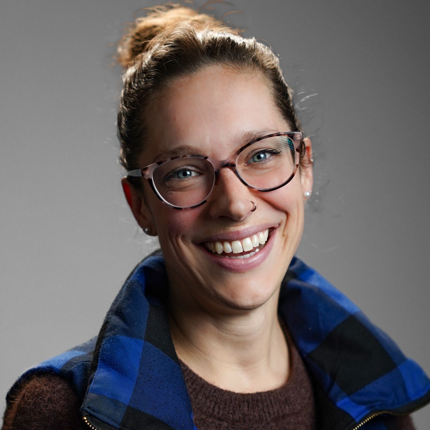 A woman wearing glasses and a plaid vest is smiling for the camera.
