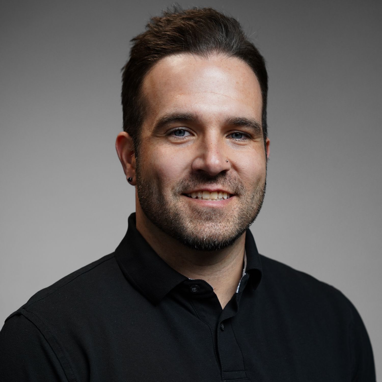 A man with a beard is wearing a black shirt and smiling for the camera.