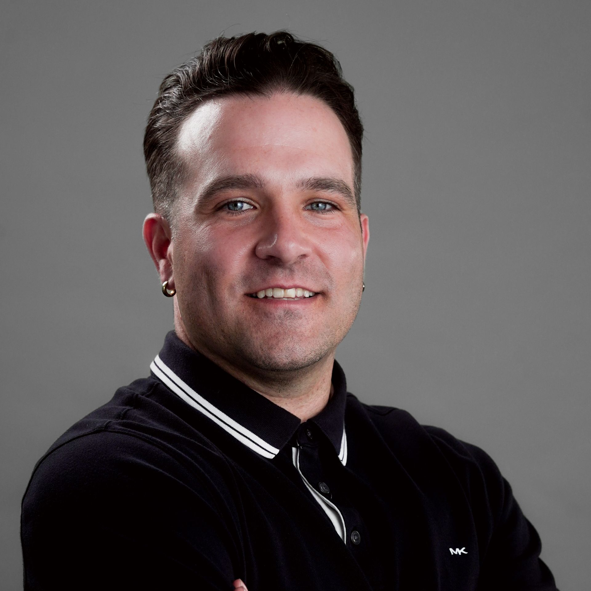 A man with a beard is wearing a black shirt and smiling for the camera.