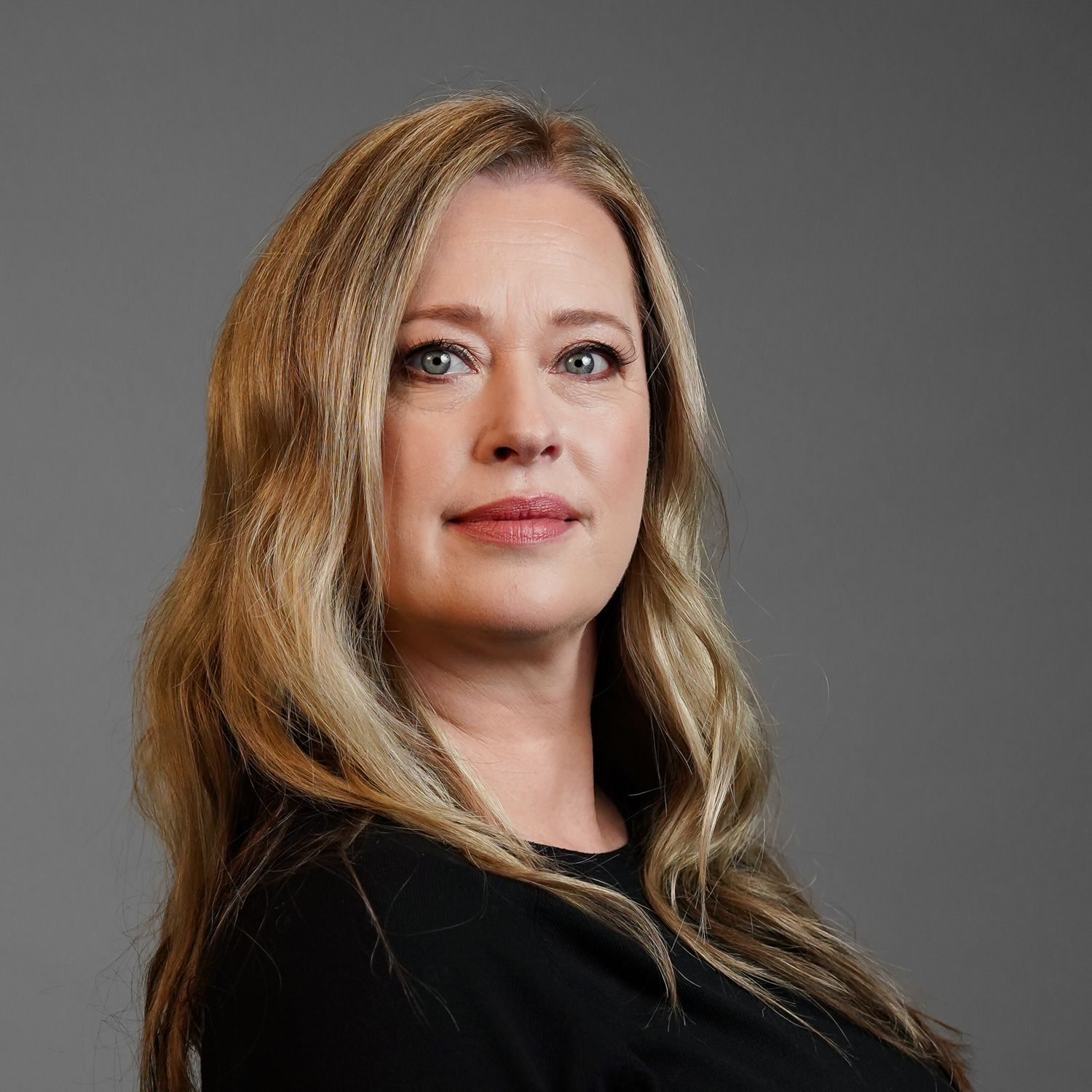 A woman with long blonde hair is wearing a black shirt and looking at the camera.