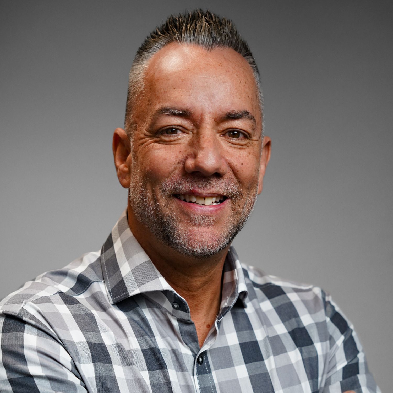 A man with a beard is wearing a plaid shirt and smiling for the camera.