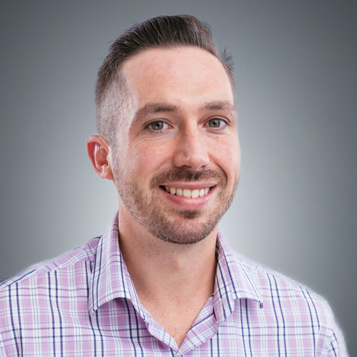 A man with a beard is wearing a plaid shirt and smiling.