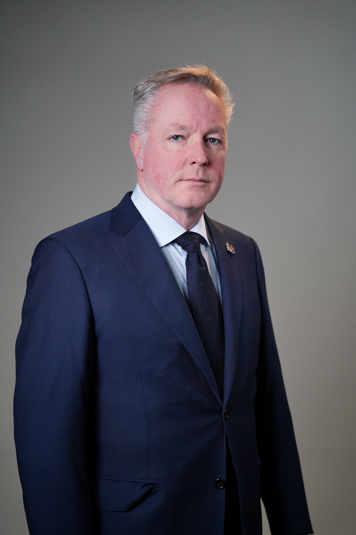 A man in a suit and tie is standing in front of a gray background.
