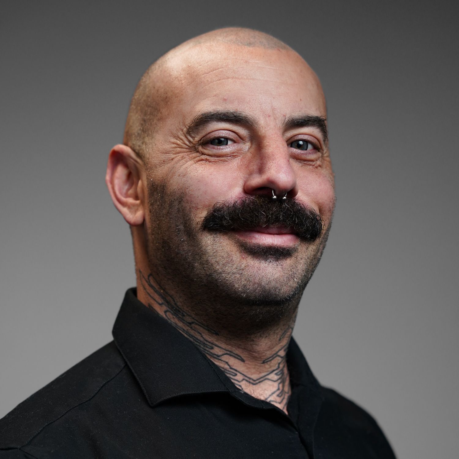 A bald man with a mustache and a tattoo on his neck is smiling.