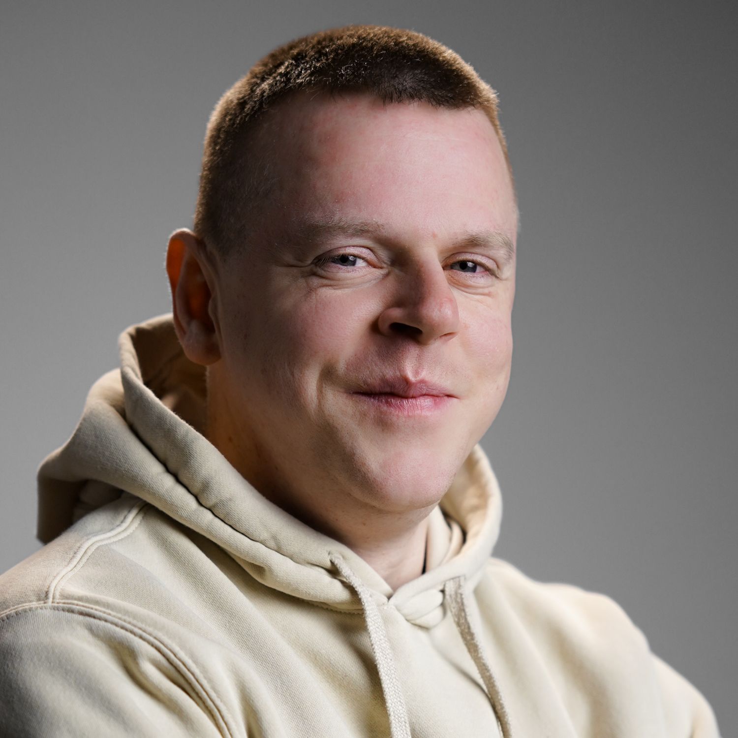 A man wearing a tan hoodie is smiling for the camera.