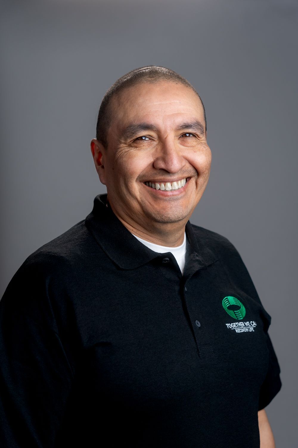 A man wearing a black polo shirt is smiling for the camera.