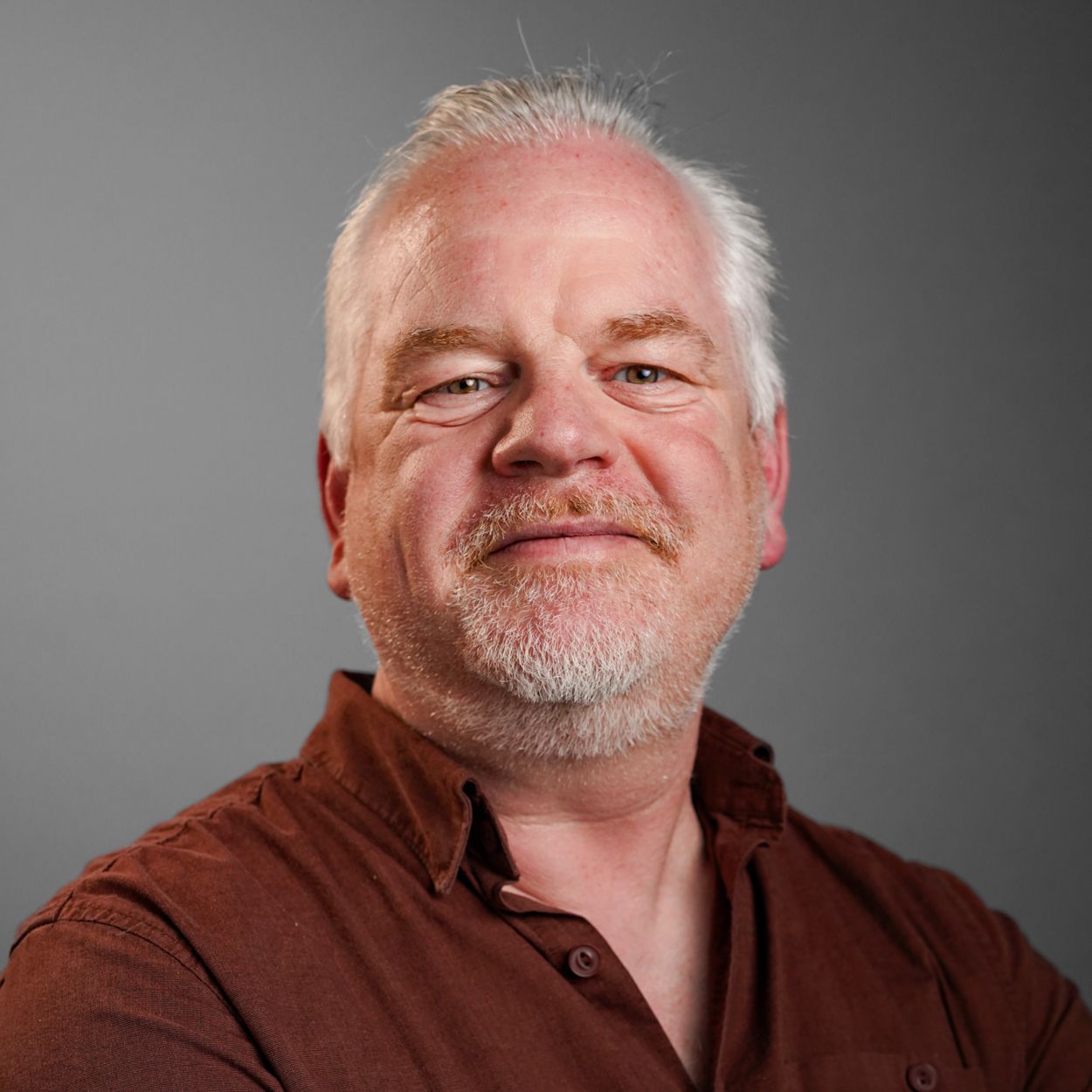 A man with a beard is wearing a brown shirt.