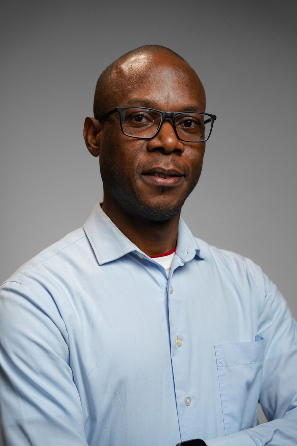 A man wearing glasses and a blue shirt is standing with his arms crossed.
