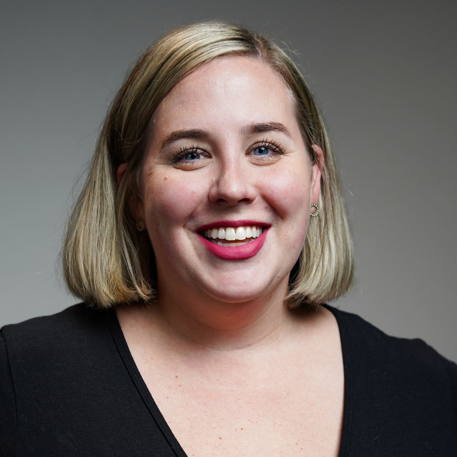 A woman wearing a black shirt and red lipstick is smiling for the camera.