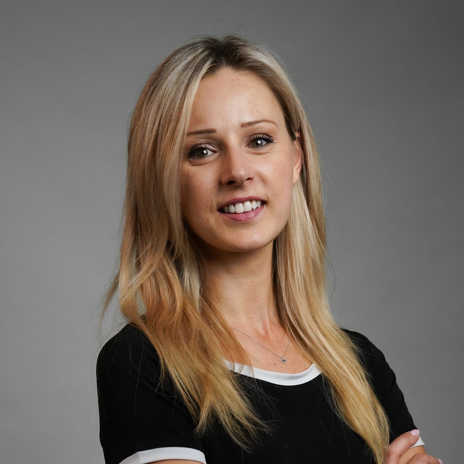 A woman with long blonde hair is wearing a black shirt and smiling.
