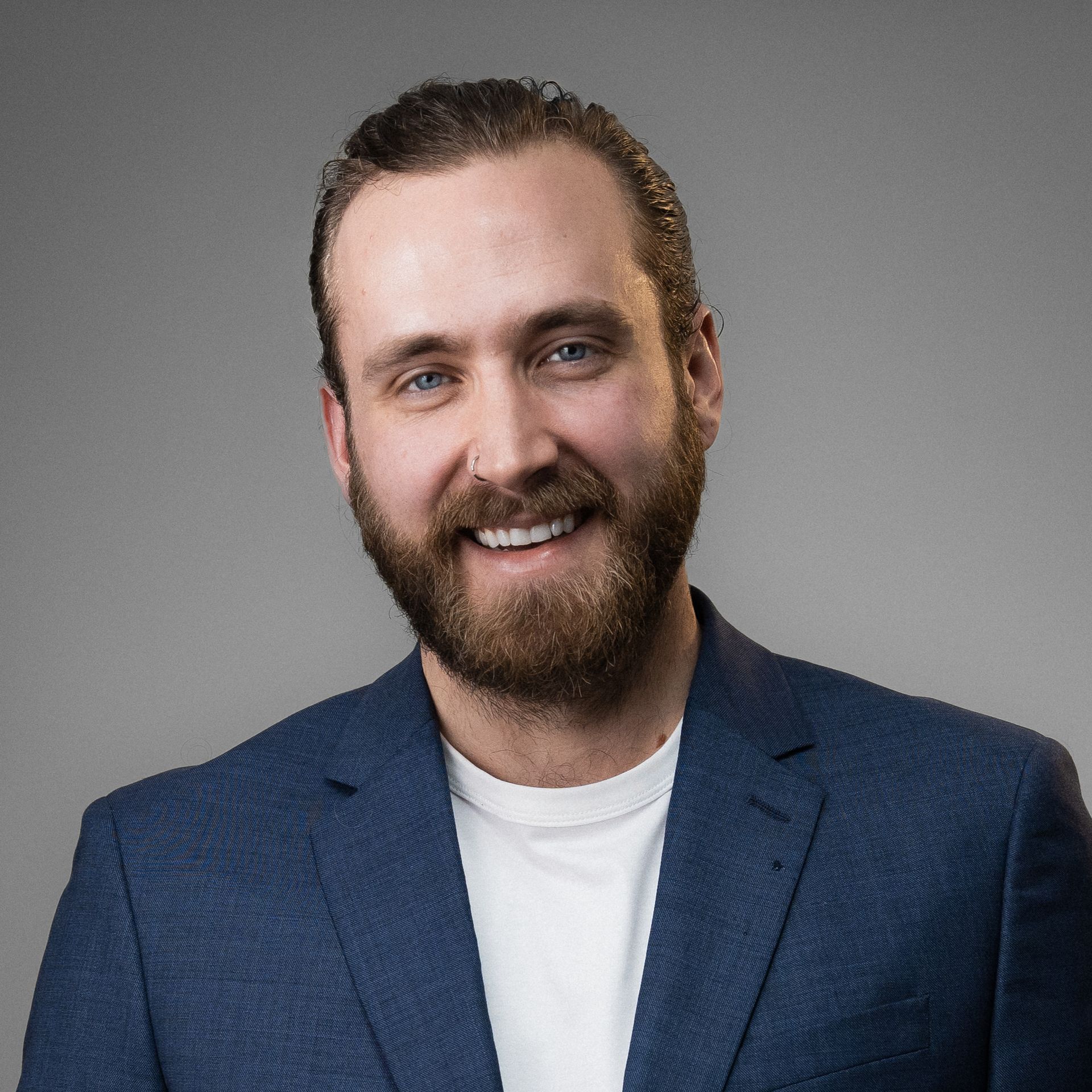 A man with a beard is wearing a blue suit and smiling.