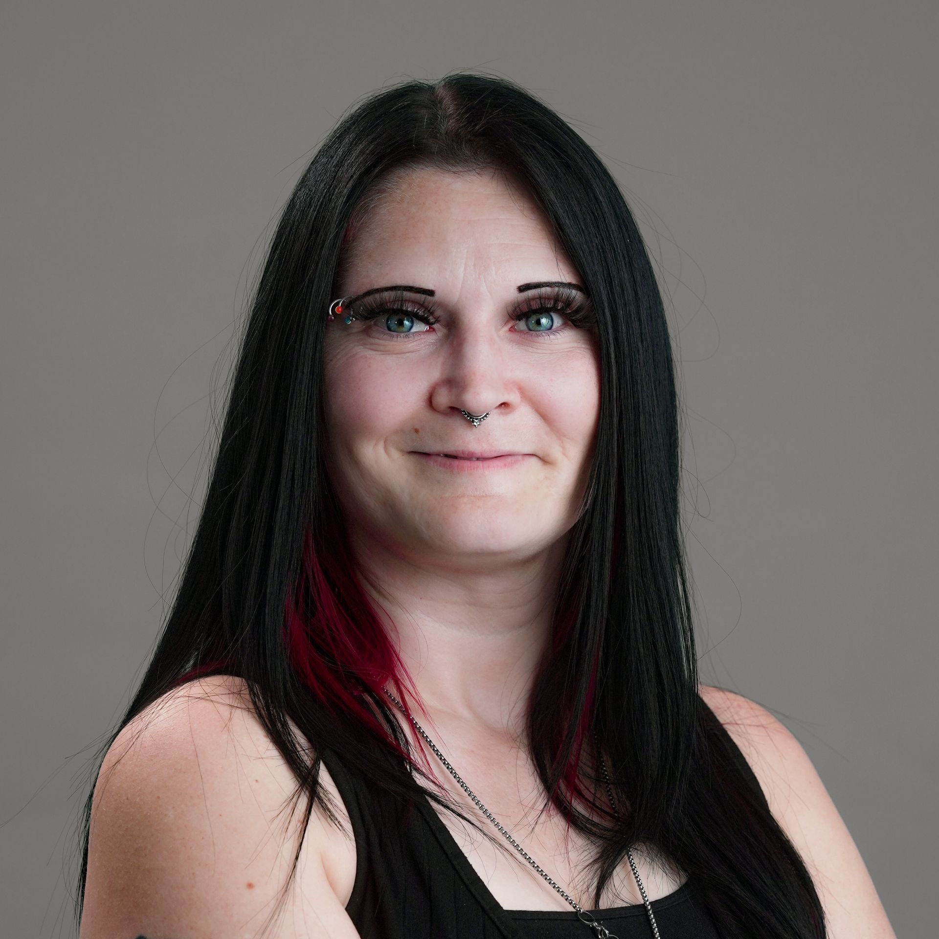 Woman with colorful braided hair and glasses smiles, wearing a black blazer.