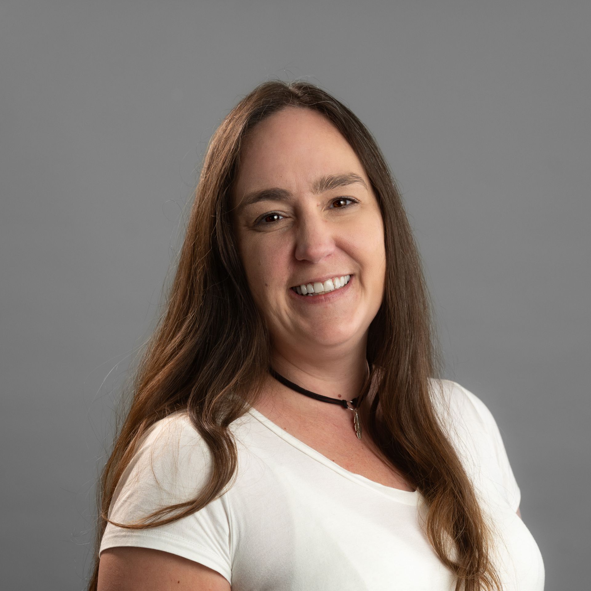 A woman with long brown hair is wearing a white shirt and smiling.