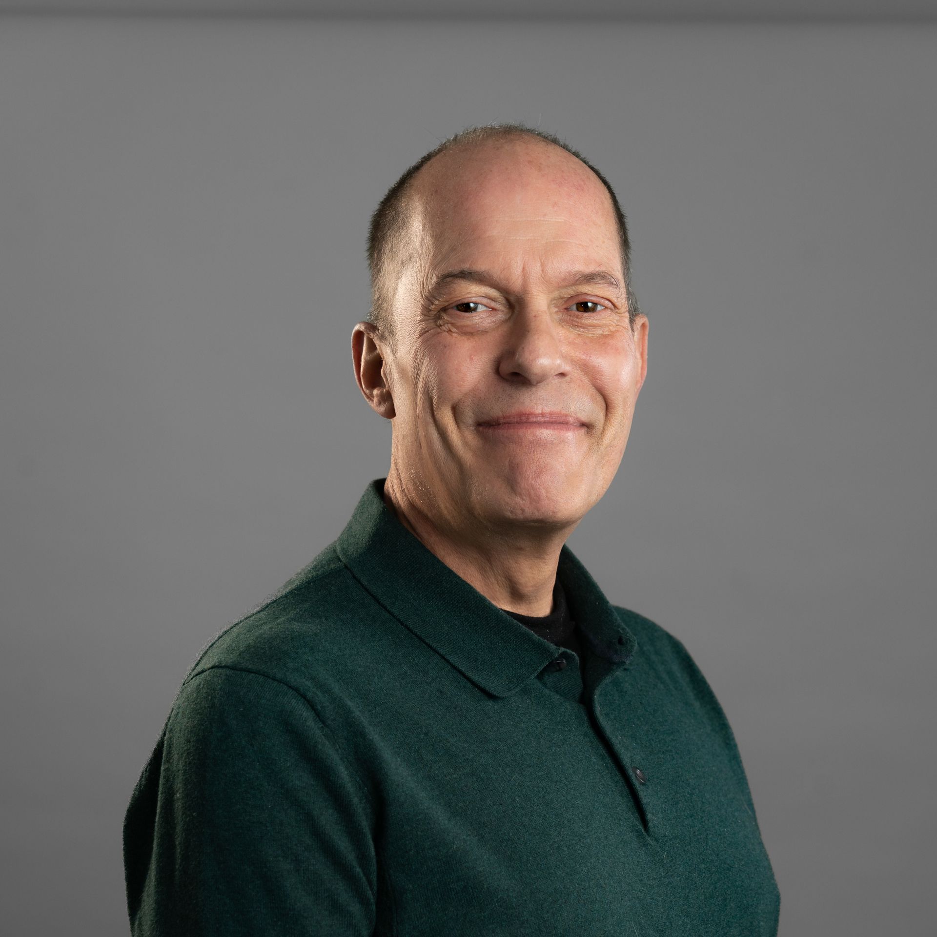 A bald man wearing a green polo shirt is smiling for the camera.