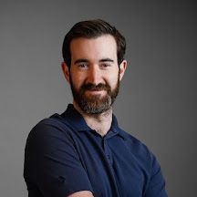 A man with a beard is wearing a blue shirt and smiling for the camera.