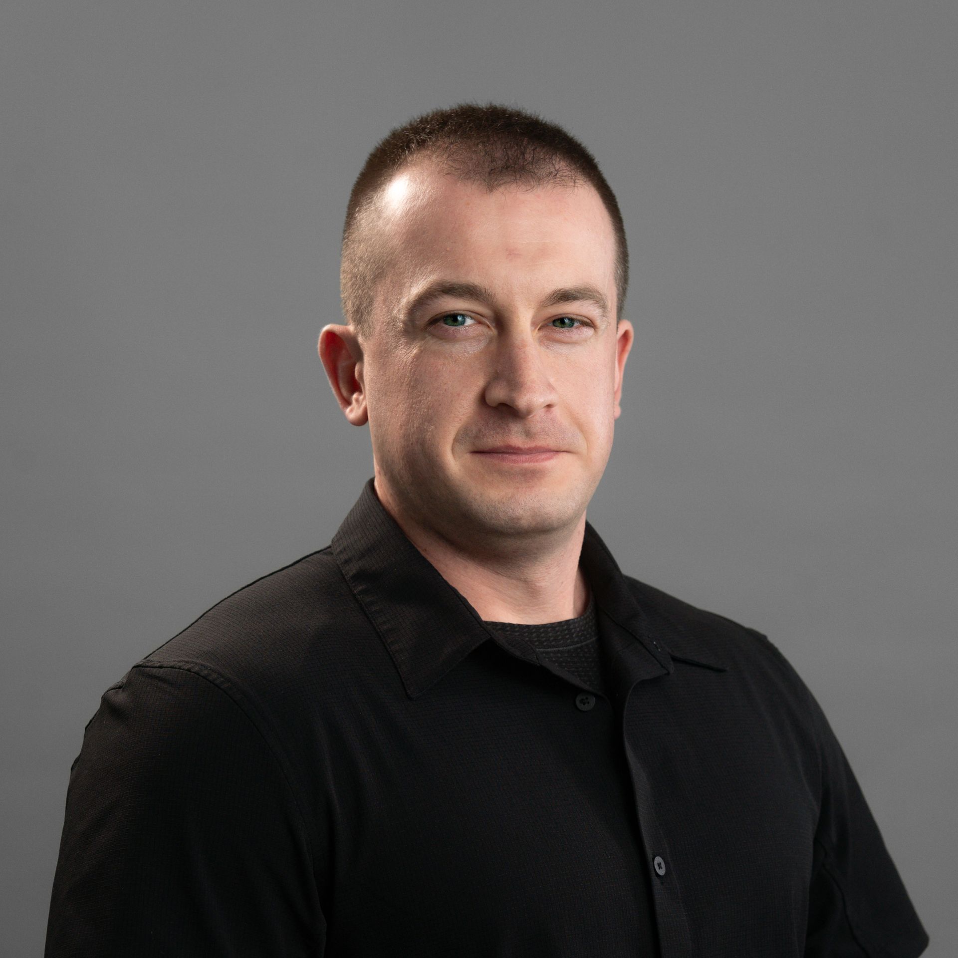 A man in a black shirt is standing in front of a gray background.