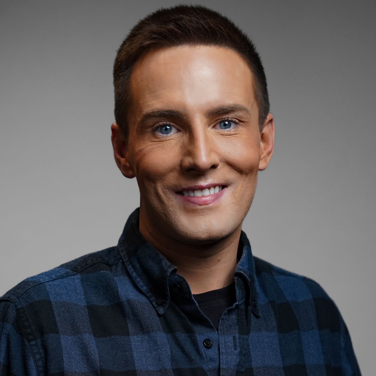 A man in a blue plaid shirt is smiling for the camera.