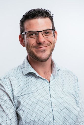 A man wearing glasses and a polka dot shirt is smiling for the camera.