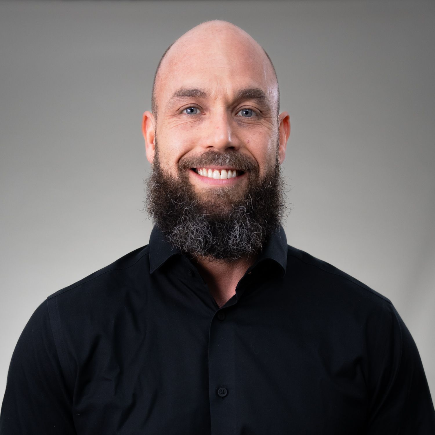 A bald man with a beard is wearing a black shirt and smiling.