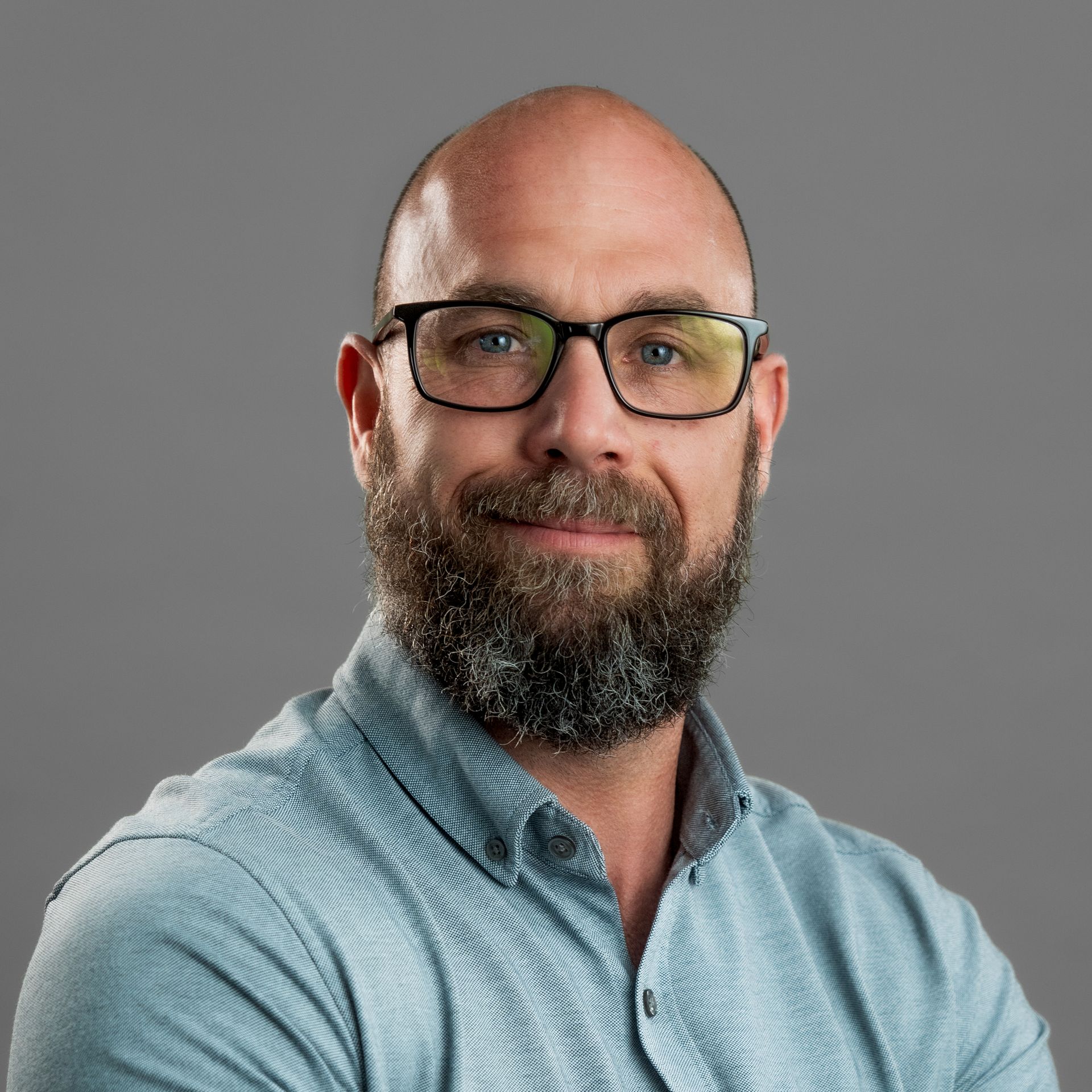 A bald man with a beard is wearing a black shirt and smiling.