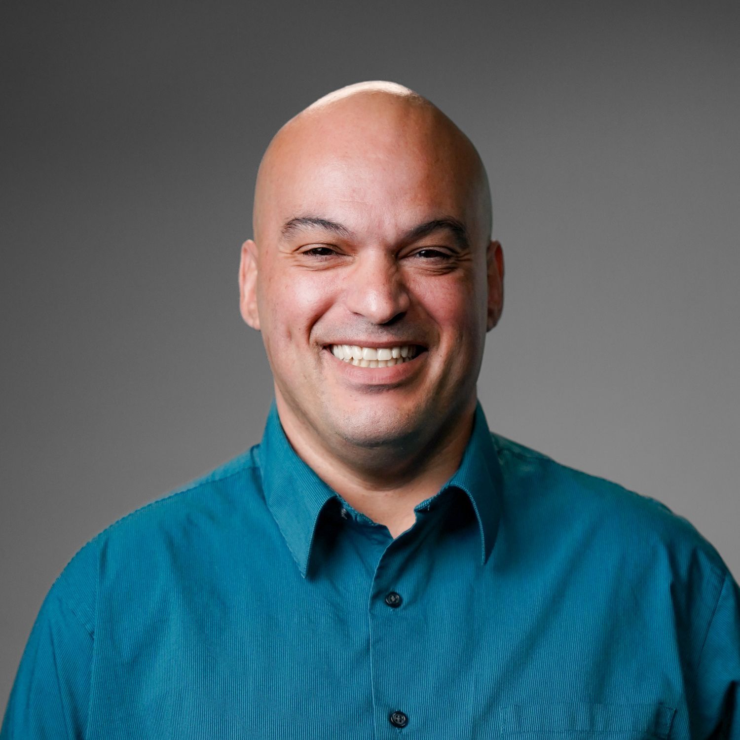 A bald man in a blue shirt is smiling for the camera.