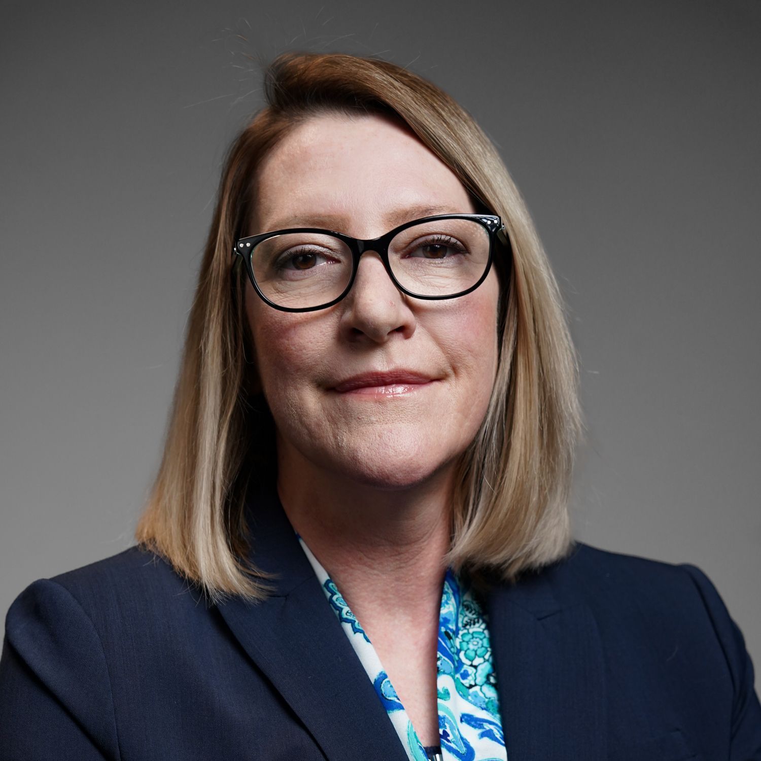 A woman wearing glasses and a suit is smiling for the camera.