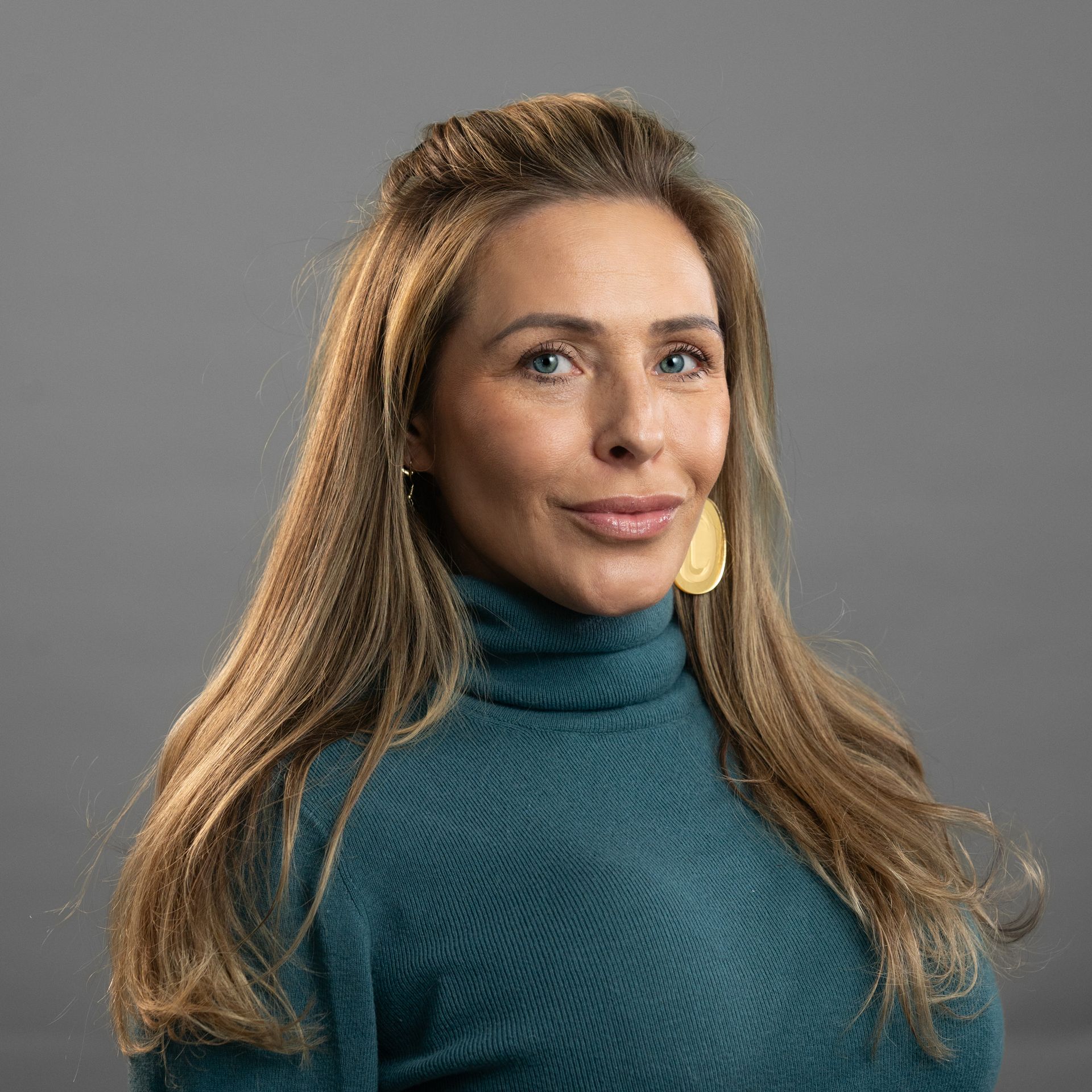 A woman with long hair is wearing a blue sweater and earrings.