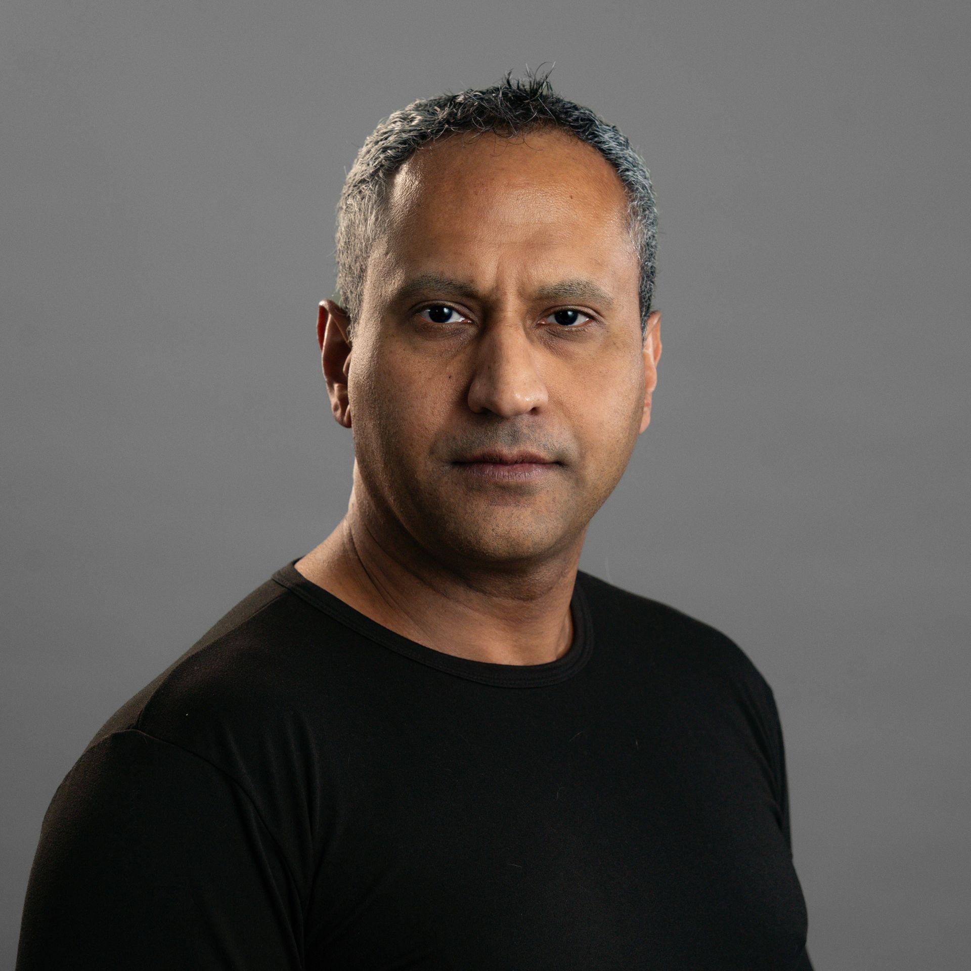 A man in a black shirt is standing in front of a gray background.