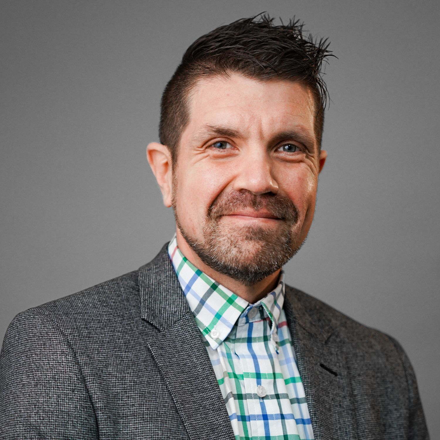A man in a suit and plaid shirt is smiling for the camera.