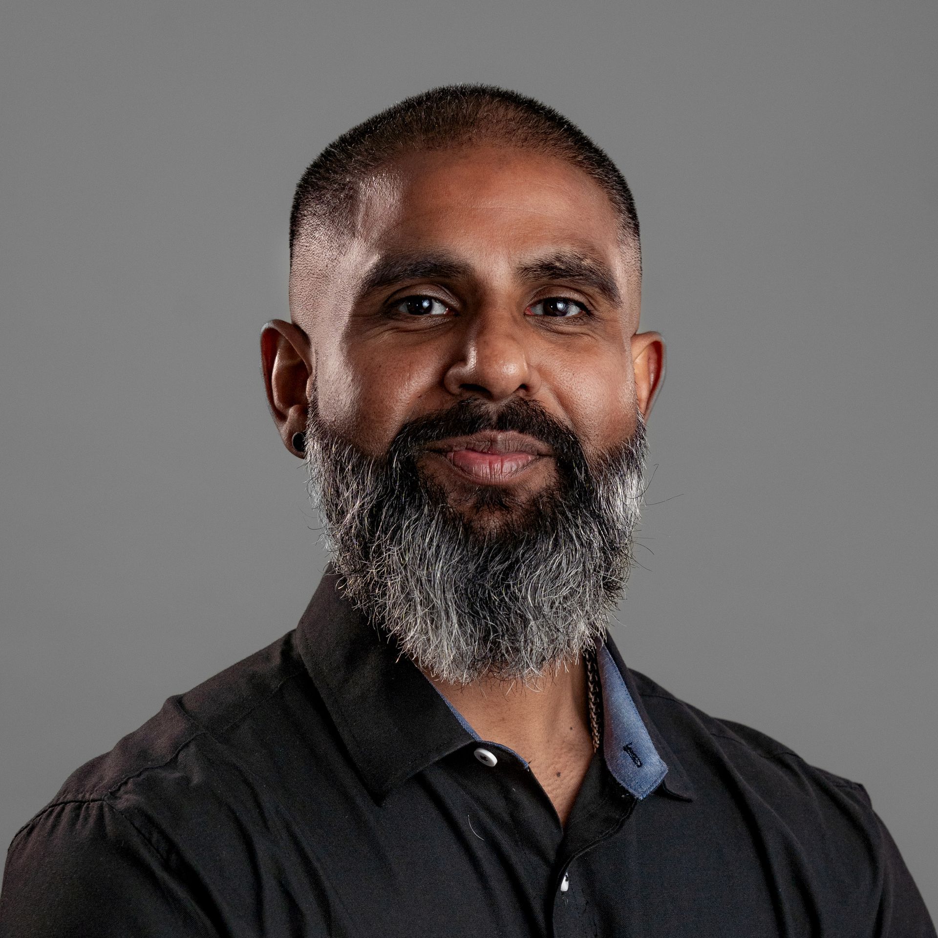 A man with a beard is wearing a black shirt and smiling.
