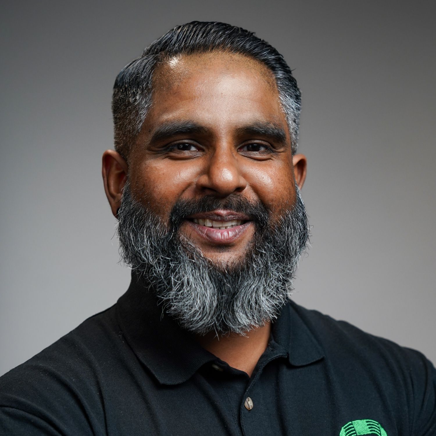 A man with a beard is wearing a black shirt and smiling.