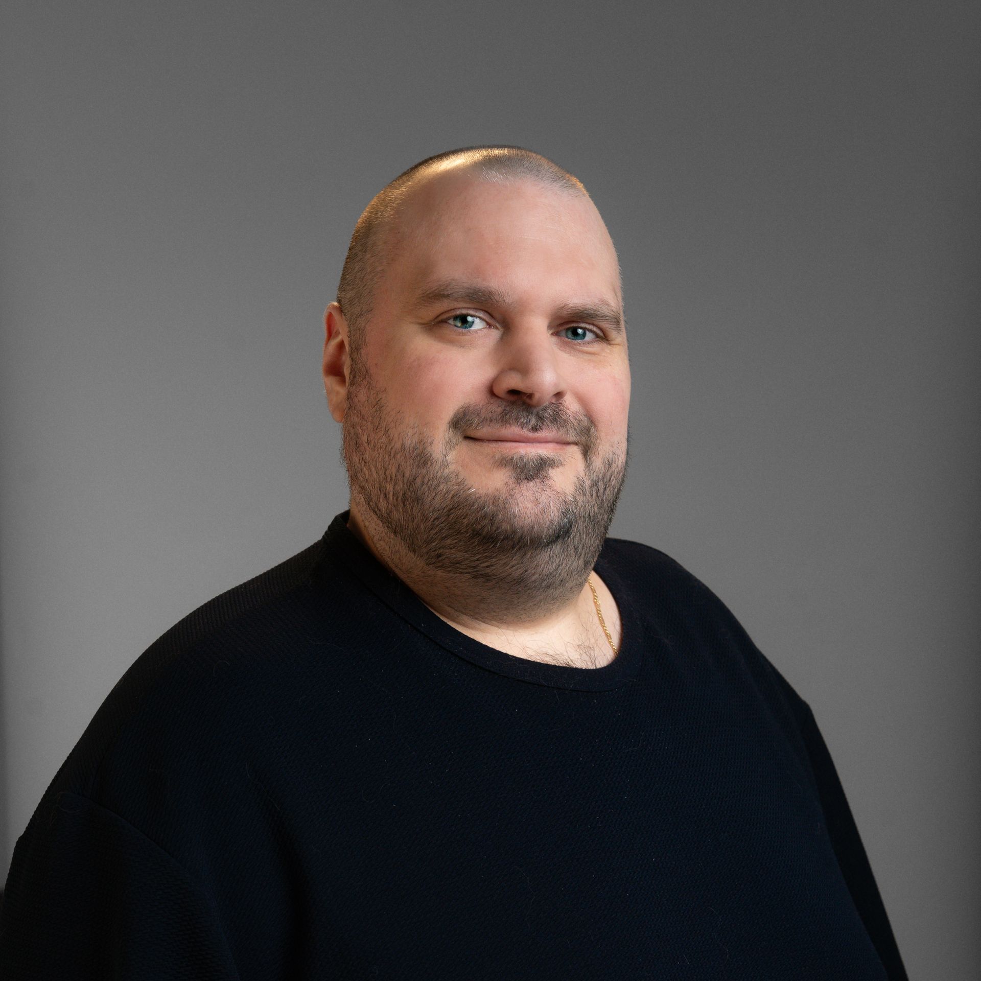 A man with a beard is wearing a black sweater and smiling for the camera.