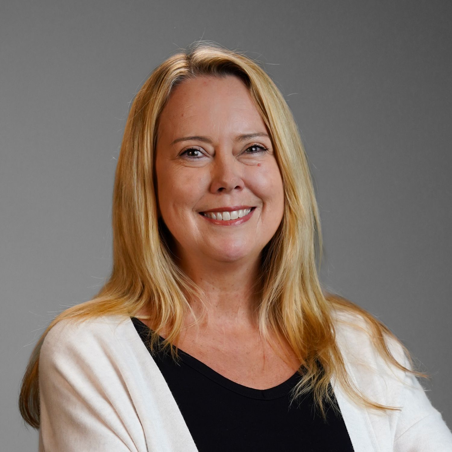 A woman wearing a white sweater and a black shirt is smiling for the camera.