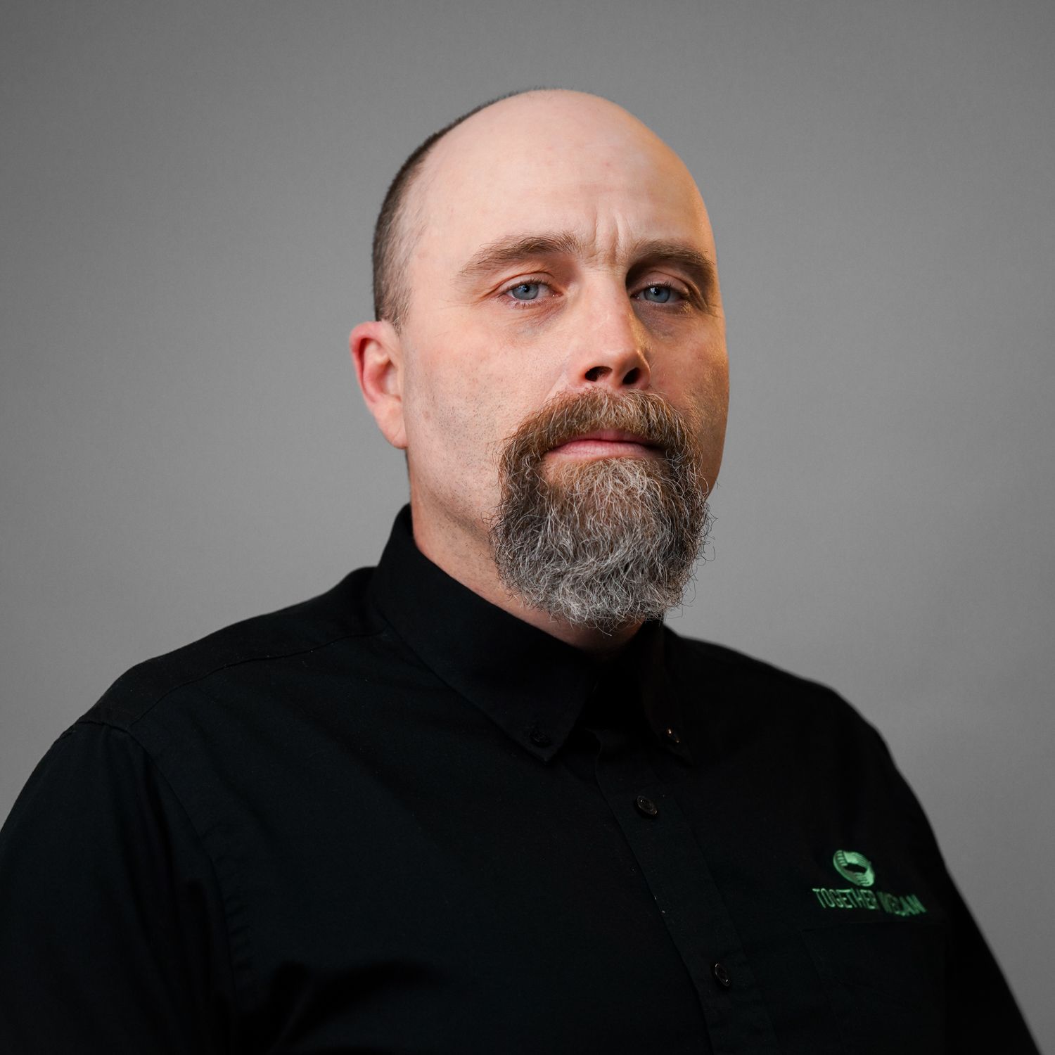 A bald man with a beard is wearing a black shirt.